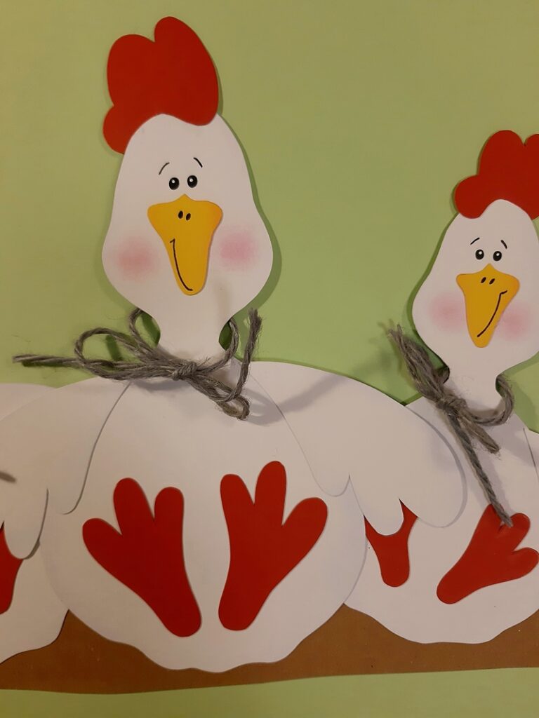 2 Hühner aus Papier sitzen auf einer Stange.
